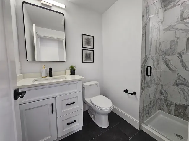 a bathroom with a toilet sink vanity granite and shower
