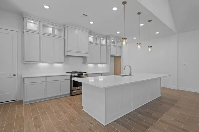 a large white kitchen with stainless steel appliances granite countertop a stove a sink a refrigerator and white cabinets with wooden floor