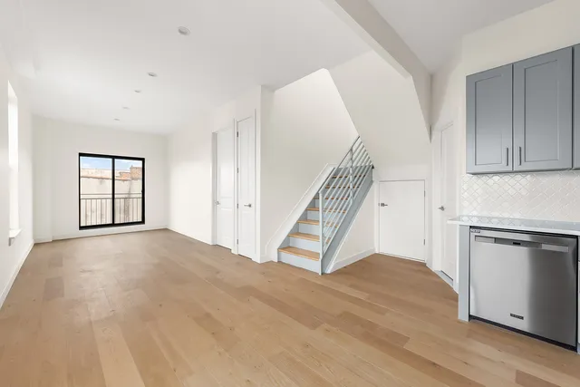 a view of an empty room with wooden floor and a kitchen