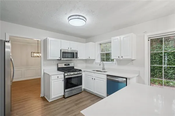 a kitchen with stainless steel appliances granite countertop a stove top oven a sink dishwasher a refrigerator and white cabinets with wooden floor