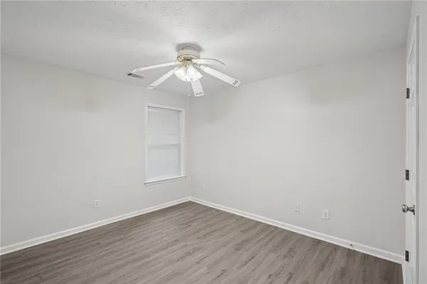 a view of an empty room with wooden floor and a ceiling fan