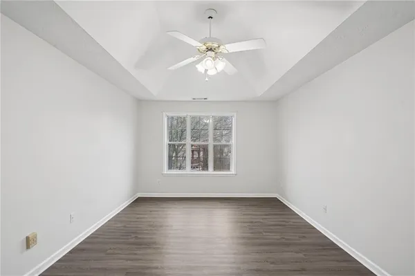 an empty room with wooden floor chandelier fan and windows