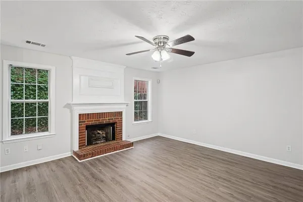 a view of an empty room with wooden floor fireplace and a window