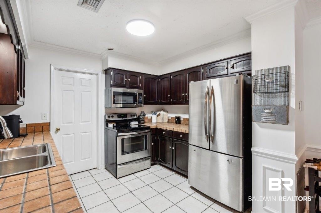 3616 Vista Ridge Drive Mobile, AL 36693 - Photo 6 of 20 Kitchen with appliances with stainless steel finishes, dark brown cabinets, crown molding, light tile patterned floors, and sink