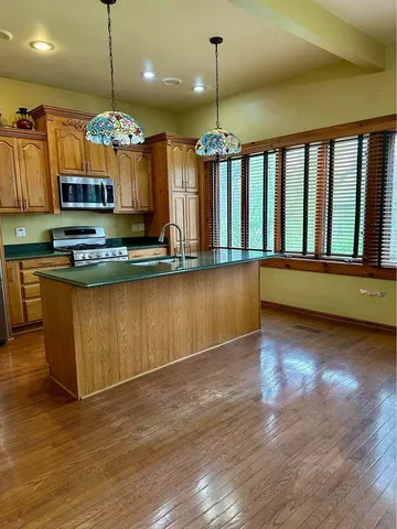 a view of a kitchen with a center island wooden floor stainless steel appliances and a chandelier