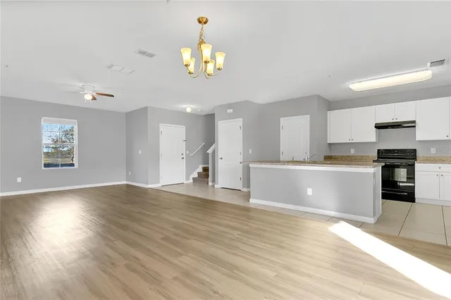 a view of an empty room and kitchen with wooden floor