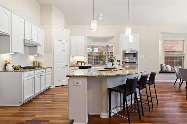 a kitchen with stainless steel appliances kitchen island granite countertop a table chairs sink and cabinets