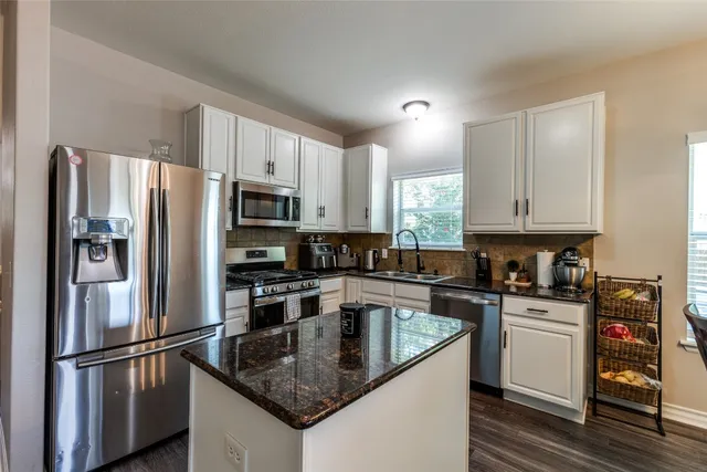 a kitchen with granite countertop a refrigerator stove and sink with wooden floor