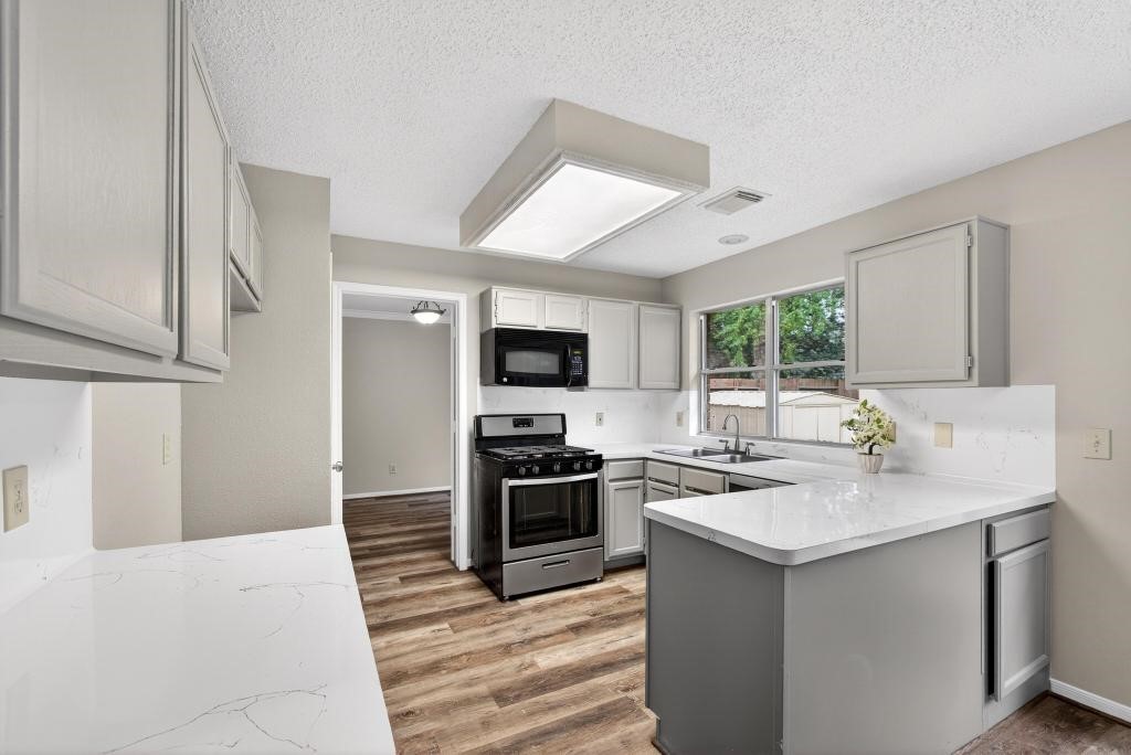 8815 Stoney Bend Drive Spring, TX 77379 - Photo 11 of 50 Modern kitchen with elegant countertops and light cabinetry. Features include a stainless steel gas stove, microwave, and dishwasher. The room is brightened by large windows and complemented by the flooring.