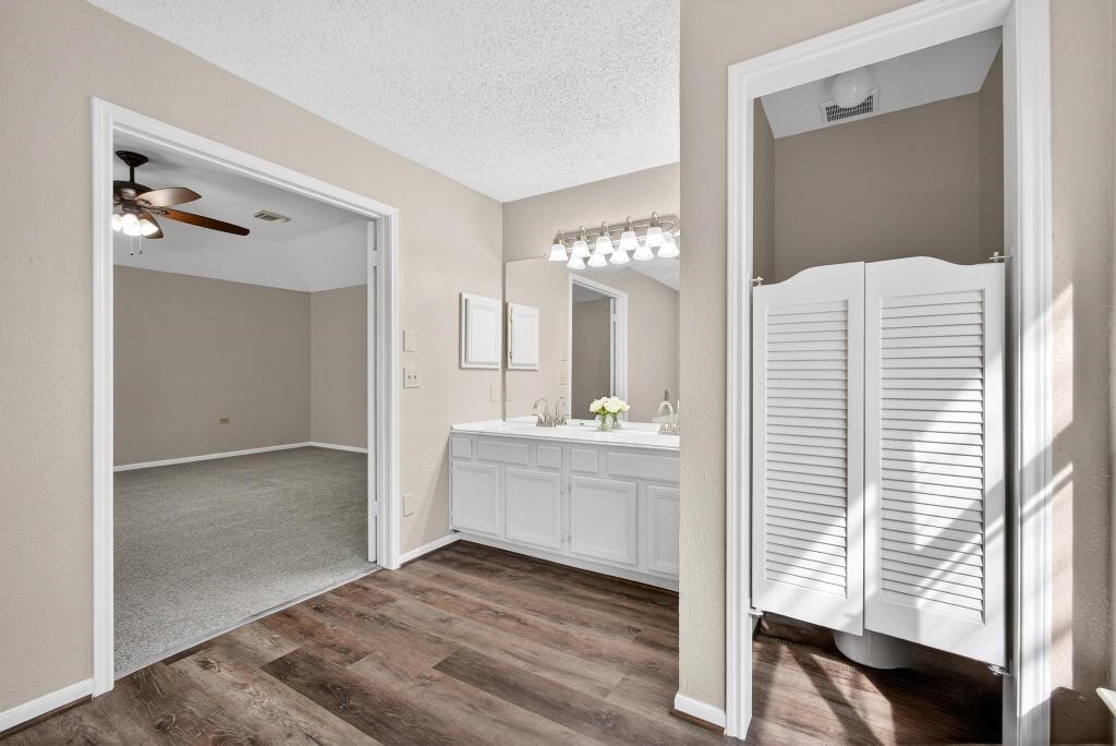 8815 Stoney Bend Drive Spring, TX 77379 - Photo 19 of 50 This photo displays a bright bathroom with a double vanity and modern lighting, adjacent to a carpeted bedroom with a ceiling fan. The space is inviting and well-lit, featuring neutral tones.