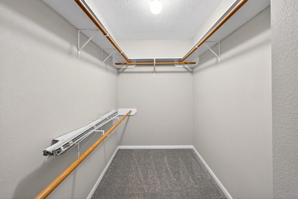 8815 Stoney Bend Drive Spring, TX 77379 - Photo 20 of 50 This photo showcases a spacious walk-in closet with ample hanging space on wooden rods, neutral walls, and carpeted flooring, perfect for organizing clothes and accessories.