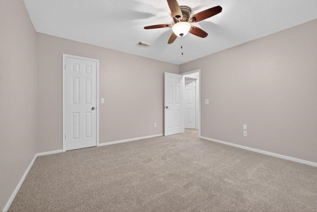 8815 Stoney Bend Drive Spring, TX 77379 - Photo 22 of 50 This is a spacious, carpeted bedroom with neutral walls and a ceiling fan. It features a closet and an adjoining door leading to another area of the home, providing a cozy and functional space.