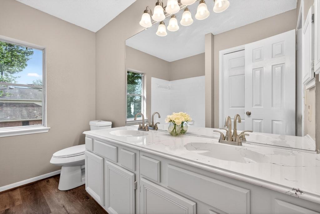 8815 Stoney Bend Drive Spring, TX 77379 - Photo 23 of 50 This bathroom features a dual-sink vanity with elegant gold fixtures, a large mirror, and modern lighting. It has a window providing natural light, neutral wall colors, and a clean, bright aesthetic.