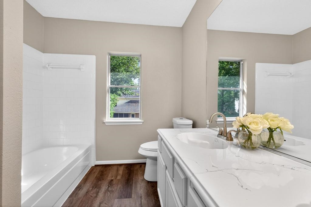 8815 Stoney Bend Drive Spring, TX 77379 - Photo 24 of 50 This bathroom features a modern, bright design with a large vanity mirror, dual sinks, and a sleek countertop. The room includes a bathtub with a tiled surround and two windows for natural light. The flooring adds warmth, complemented by neutral wall tones.