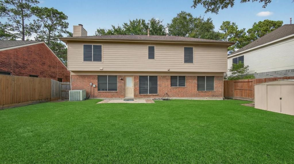 8815 Stoney Bend Drive Spring, TX 77379 - Photo 30 of 50 This photo shows the backyard of a two-story home with a well-maintained lawn. The house features a combination of brick and siding, with several windows on both levels. It has a small patio area and is enclosed by a wooden fence, providing privacy.