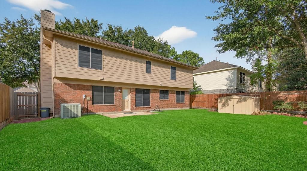 8815 Stoney Bend Drive Spring, TX 77379 - Photo 31 of 50 Spacious backyard with lush green lawn, fenced for privacy. The house features a two-story exterior with a mix of brick and siding, large windows, and a small storage shed. Ideal for outdoor activities and relaxation.