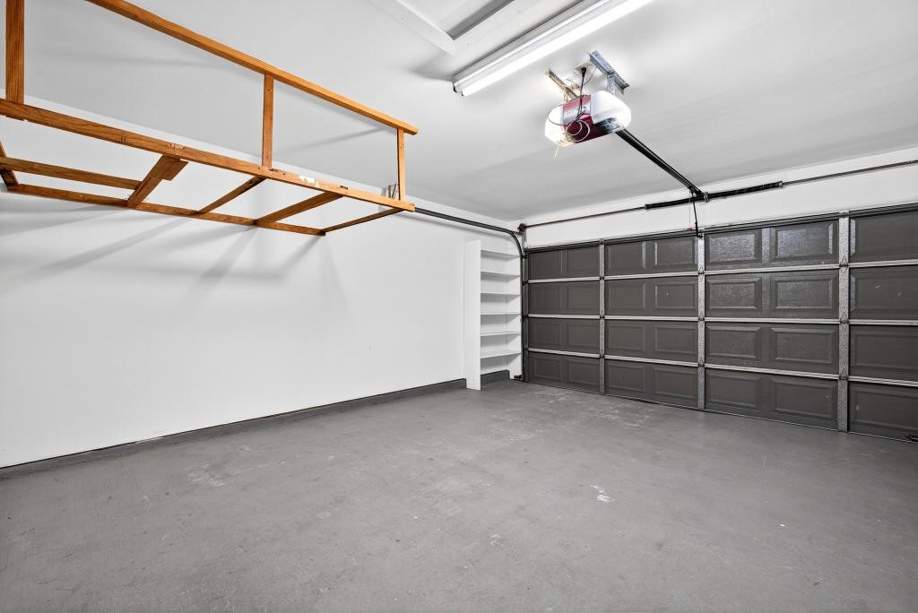 8815 Stoney Bend Drive Spring, TX 77379 - Photo 32 of 50 This photo shows a spacious, clean garage with a dark-paneled door, overhead storage, and shelving, ideal for parking and extra storage.