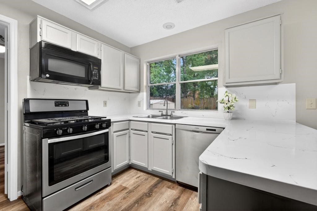 8815 Stoney Bend Drive Spring, TX 77379 - Photo 9 of 50 This kitchen features modern stainless steel appliances, including a gas stove and dishwasher. It has white cabinetry, light countertops, and a window offering natural light and a view of the backyard.