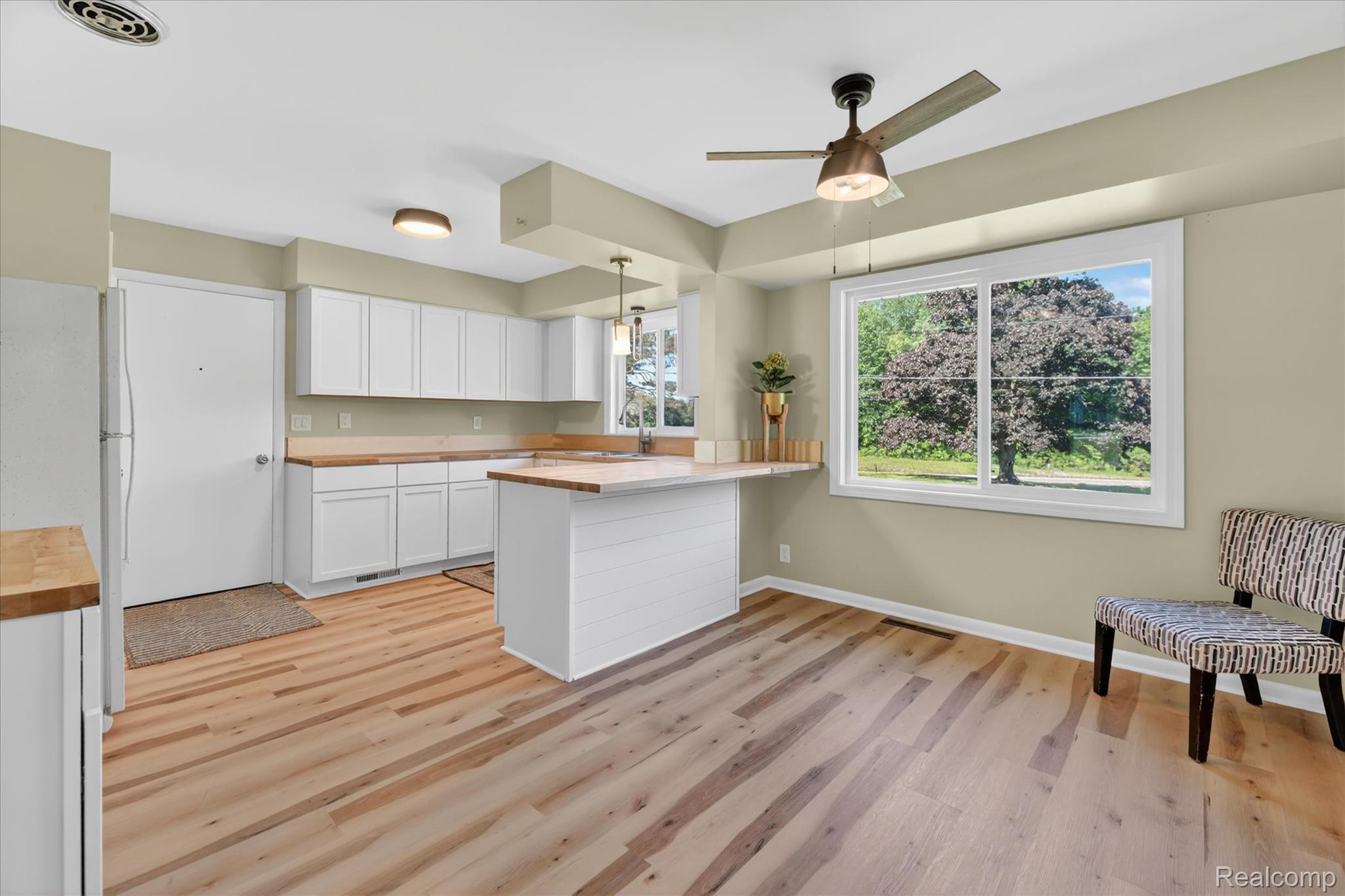 2250 Montague Road Davison, MI 48423 - Photo 13 of 45 Kitchen featuring light wood-finish flooring, white cabinetry, light wood countertops, a center island with breakfast bar, and a large window overlooking exterior trees