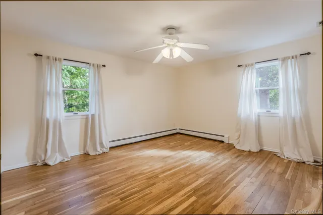 an empty room with wooden floor chandelier fan and windows