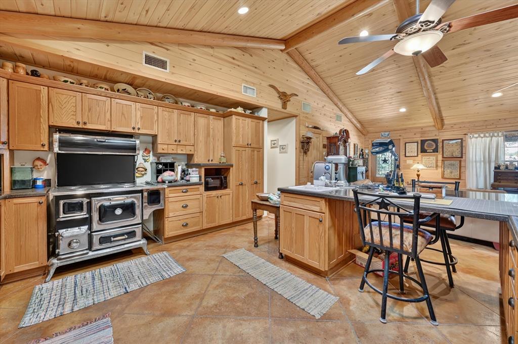 1623 3 Skillet Road Springtown, TX 76082 - Photo 20 of 40 Vaulted wood-paneled ceiling with exposed beams, wood-finish cabinetry, built-in range, and a kitchen island with seating
