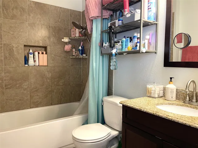 a bathroom with a granite countertop bathtub sink vanity mirror and toilet