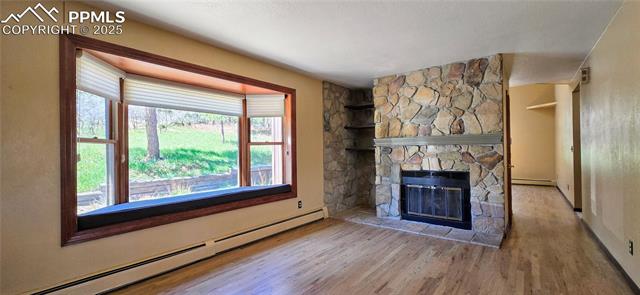 18170 Forest View Road Monument, CO 80132 - Photo 4 of 32 Unfurnished living room featuring a baseboard radiator, wood finished floors, a fireplace, and baseboards