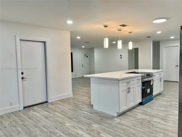 a large white kitchen with a large counter top stainless steel appliances and wooden floor
