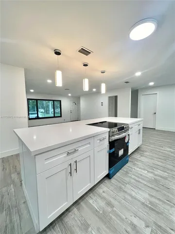 a large white kitchen with a white countertops a stove a dining table and chairs with wooden floor