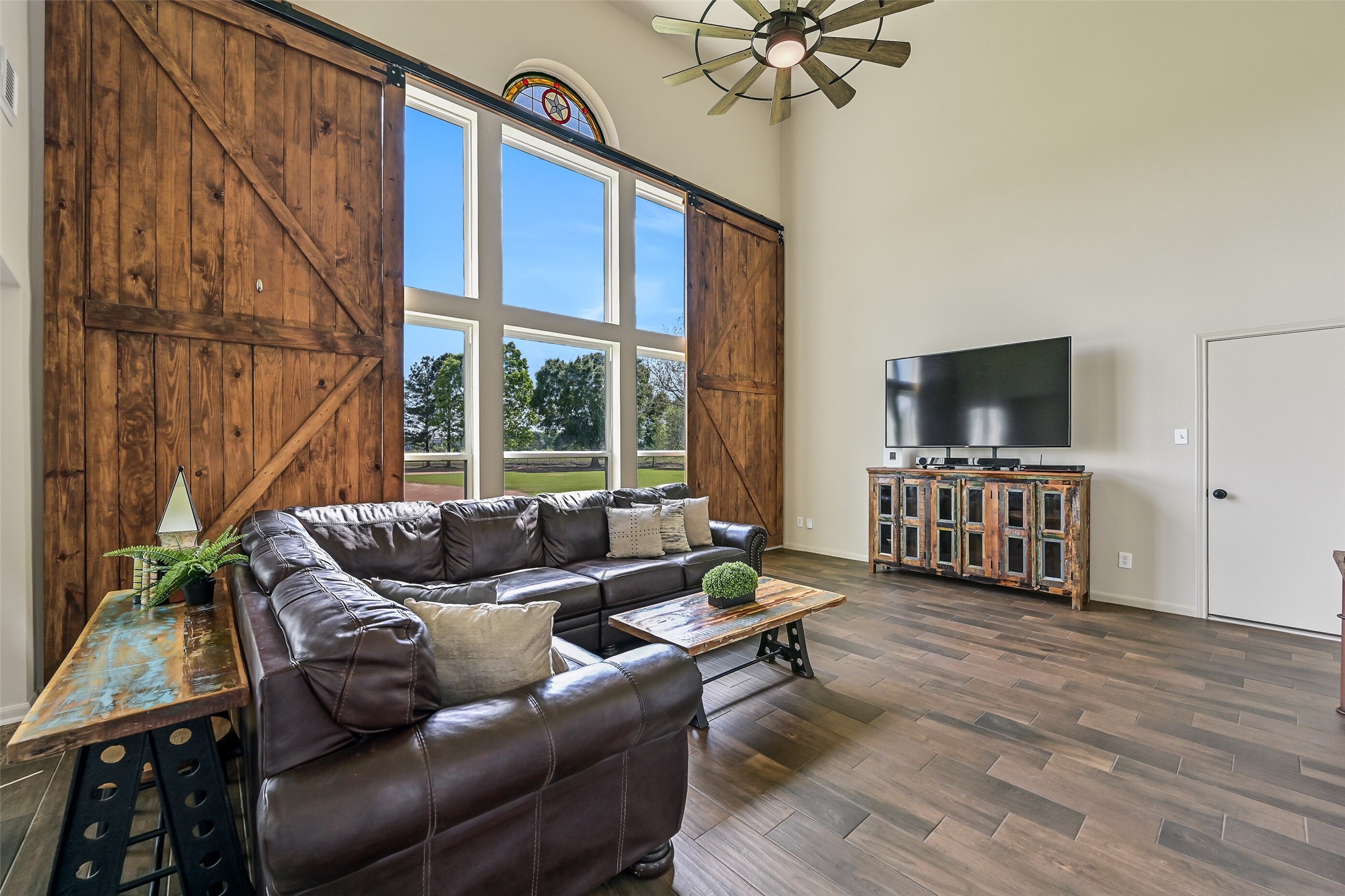 1404 Hollier Road Friendswood, TX 77546 - Photo 13 of 46 Continue into the impressive family room with soaring 18’ ceilings and expansive windows that flood the space with natural light. Custom sliding barn doors add character and function, framing views of the baseball diamond and open pasture beyond.