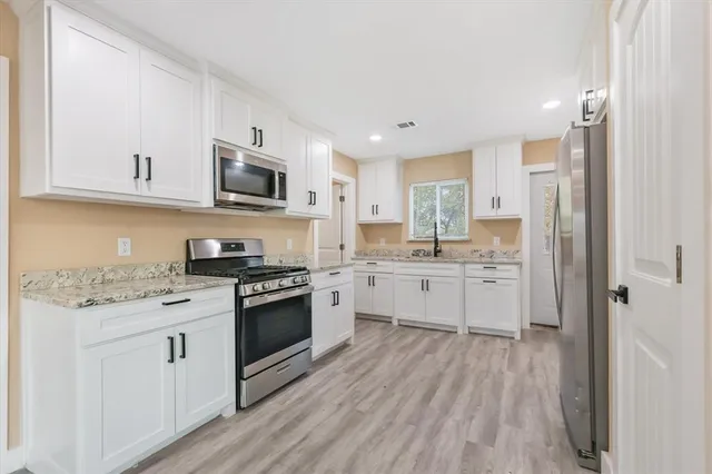 a kitchen with stainless steel appliances granite countertop a stove top oven a sink dishwasher and a refrigerator with wooden floor