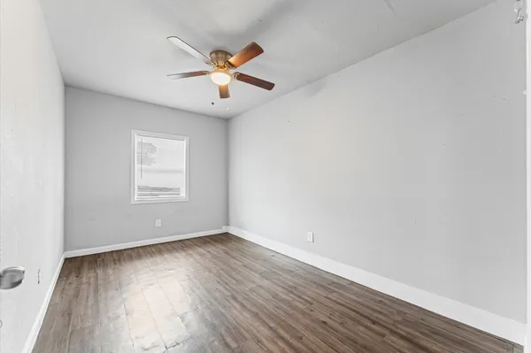 an empty room with wooden floor fan and windows