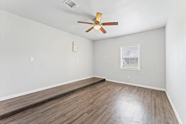 an empty room with wooden floor ceiling fan and windows