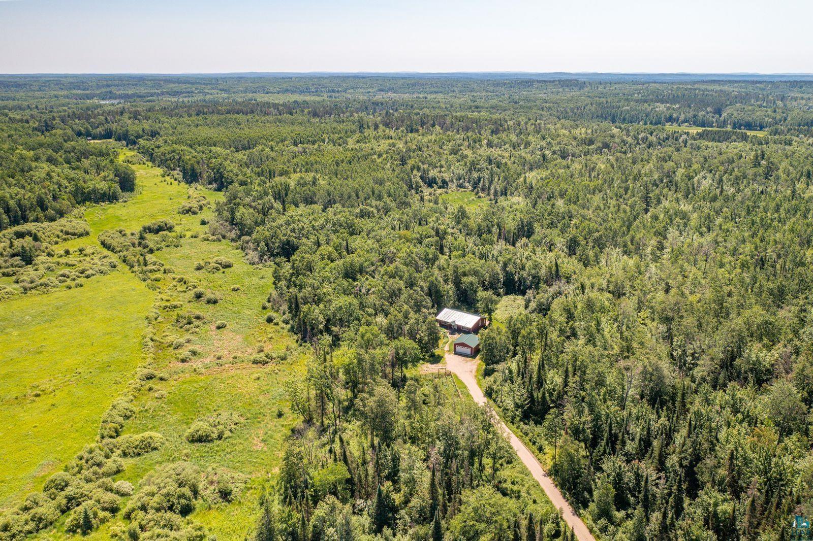 9734 Alango Road Angora, MN 55703 - Photo 33 of 41 Expansive treed acreage featuring a primary residence with a red roof, a detached green-roofed outbuilding, and a winding driveway