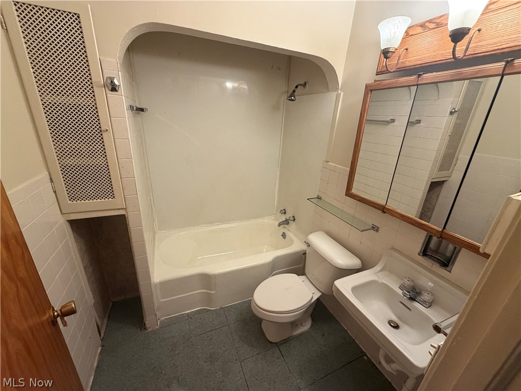 15300 Waterloo Road, Unit 1 Cleveland, OH 44110 - Photo 8 of 11 Bathroom featuring a built-in bathtub with shower, white tile surround, and an integrated storage cabinet