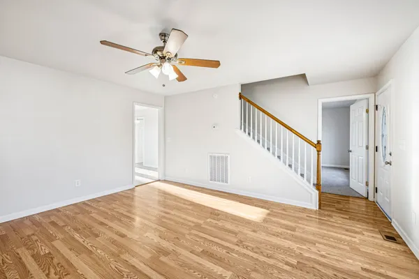 a view of an empty room with wooden floor and a ceiling fan