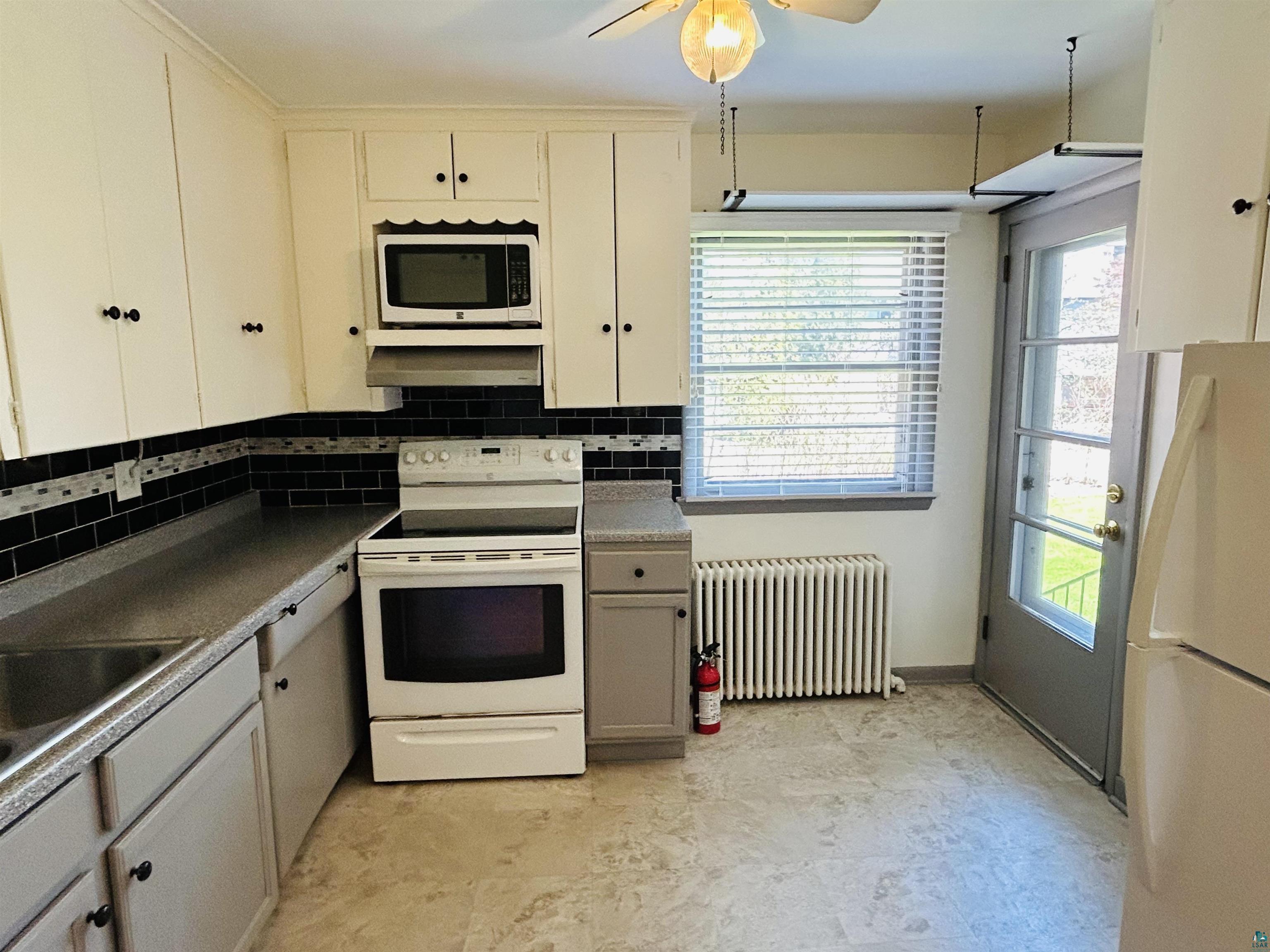 5090 London Road, Unit 1 Duluth, MN 55804 - Photo 8 of 54 Kitchen featuring white cabinetry, a black subway tile backsplash with a decorative accent band, integrated microwave, an electric range, and light-toned flooring