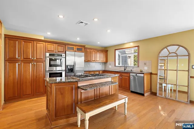 a kitchen with stainless steel appliances granite countertop a stove a sink dishwasher a refrigerator and wooden cabinets with wooden floor