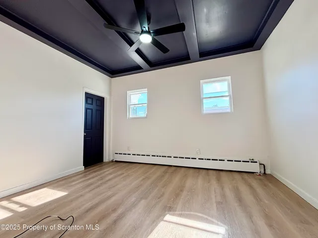 an empty room with wooden floor chandelier fan and windows
