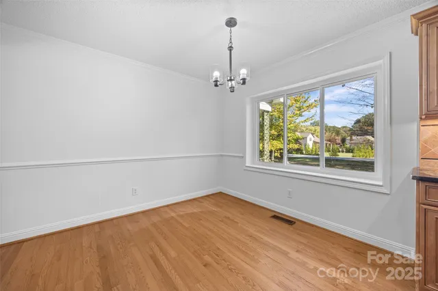 an empty room with wooden floor chandelier and windows