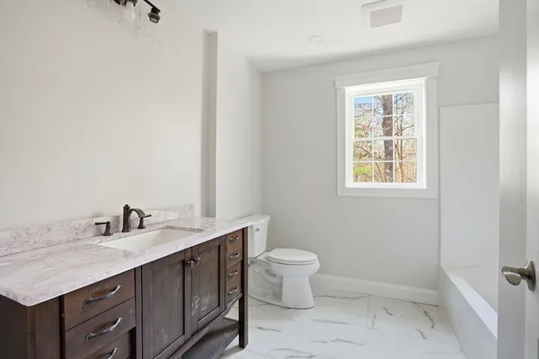 a bathroom with a granite countertop sink a toilet and a window