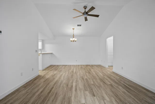 an empty room with wooden floor ceiling fan and windows