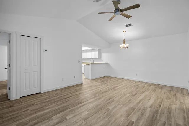 an empty room with wooden floor ceiling fan and windows