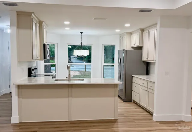 a kitchen with stainless steel appliances granite countertop a refrigerator a sink a stove and white cabinets with wooden floor