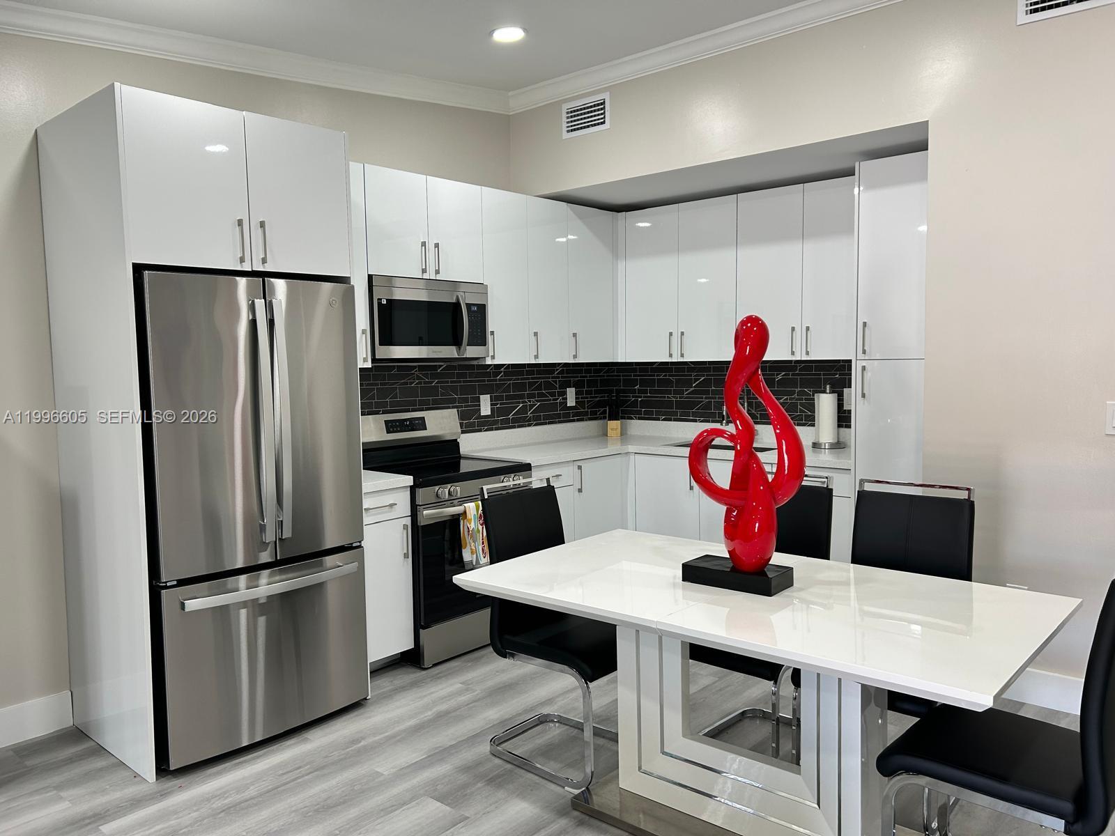 9922 Southwest 2nd Street, Unit A Miami, FL 33174 - Photo 3 of 24 a kitchen with stainless steel appliances a dining table chairs refrigerator and microwave
