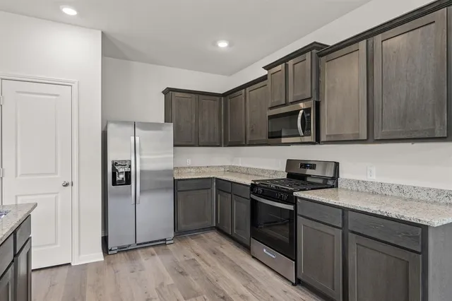 a kitchen with granite countertop a refrigerator a sink a stove a microwave and wooden cabinets