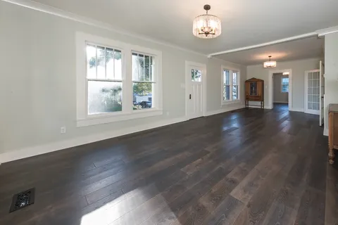 an empty room with wooden floor chandelier and windows