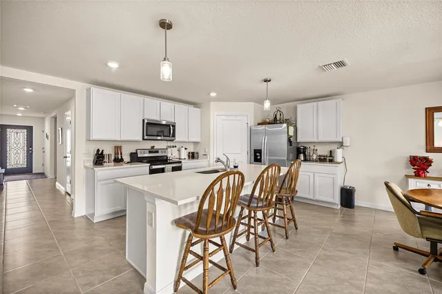 a kitchen with stainless steel appliances granite countertop a stove top oven a sink a refrigerator with a dining table and chairs