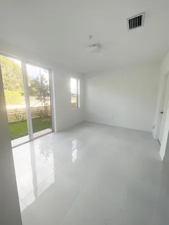 an empty room with windows and view of kitchen