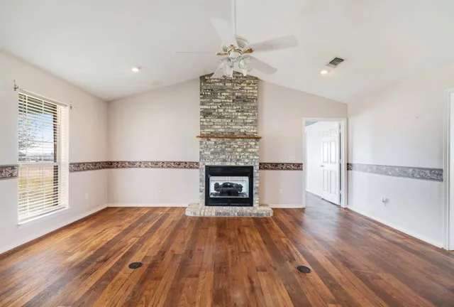 an empty room with wooden floor fireplace and windows